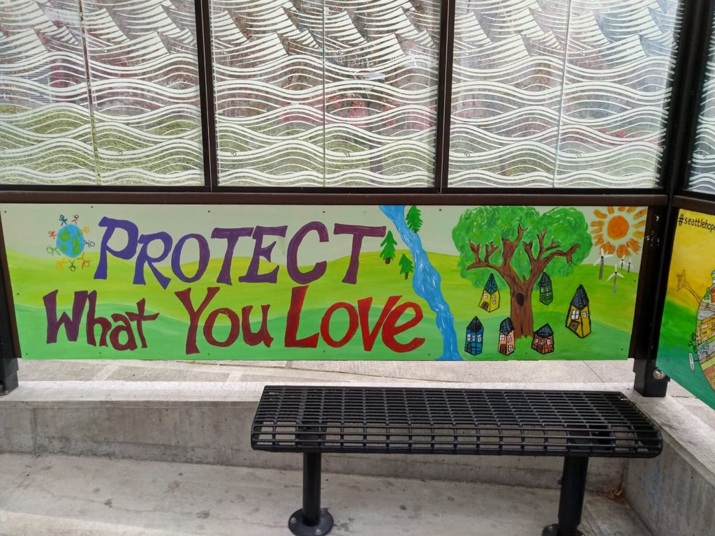 Image description: The inside of a bus shelter, with a nature scene and the words "protect what you love" painted on the back panel