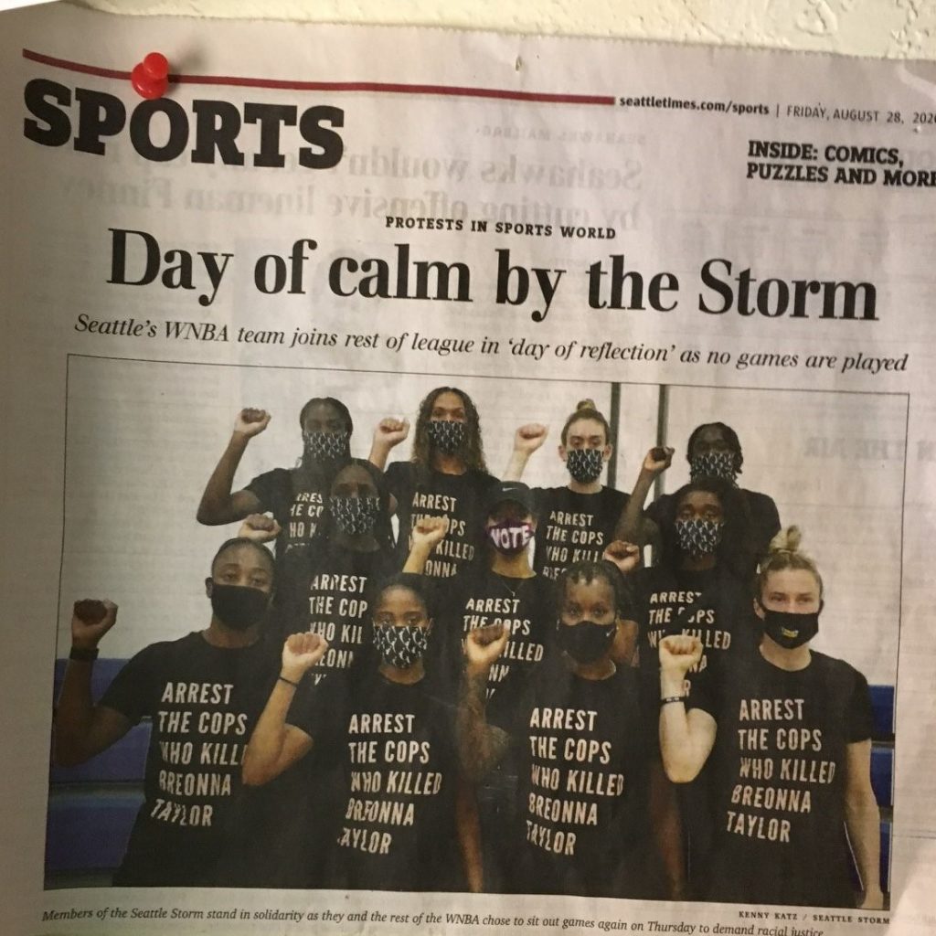 Image description: 10 women, members of the Seattle Storm basketball team, of different ages, sizes and races. All are raising their right fists and wearing Covid masks and t-shirts that say, "Arrest the cops that killed Breonna Taylor."