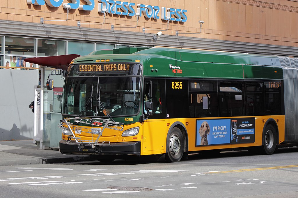 A King County Metro bus stopped at a bus stop. The words "essential trips only" show up in the bus's lighted display.