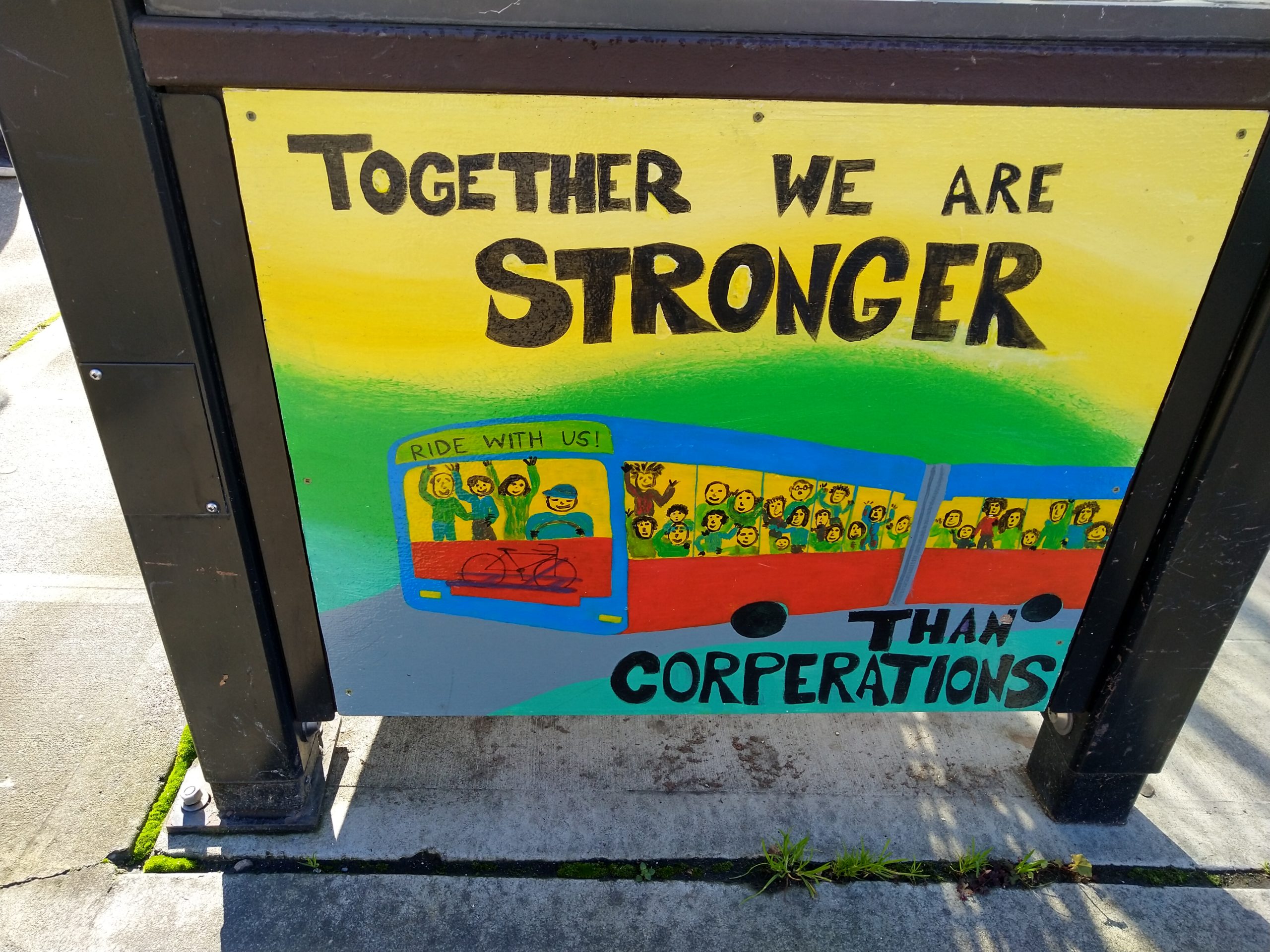 A bus shelter mural made by students. Text says, "Together we are stronger than corporations."