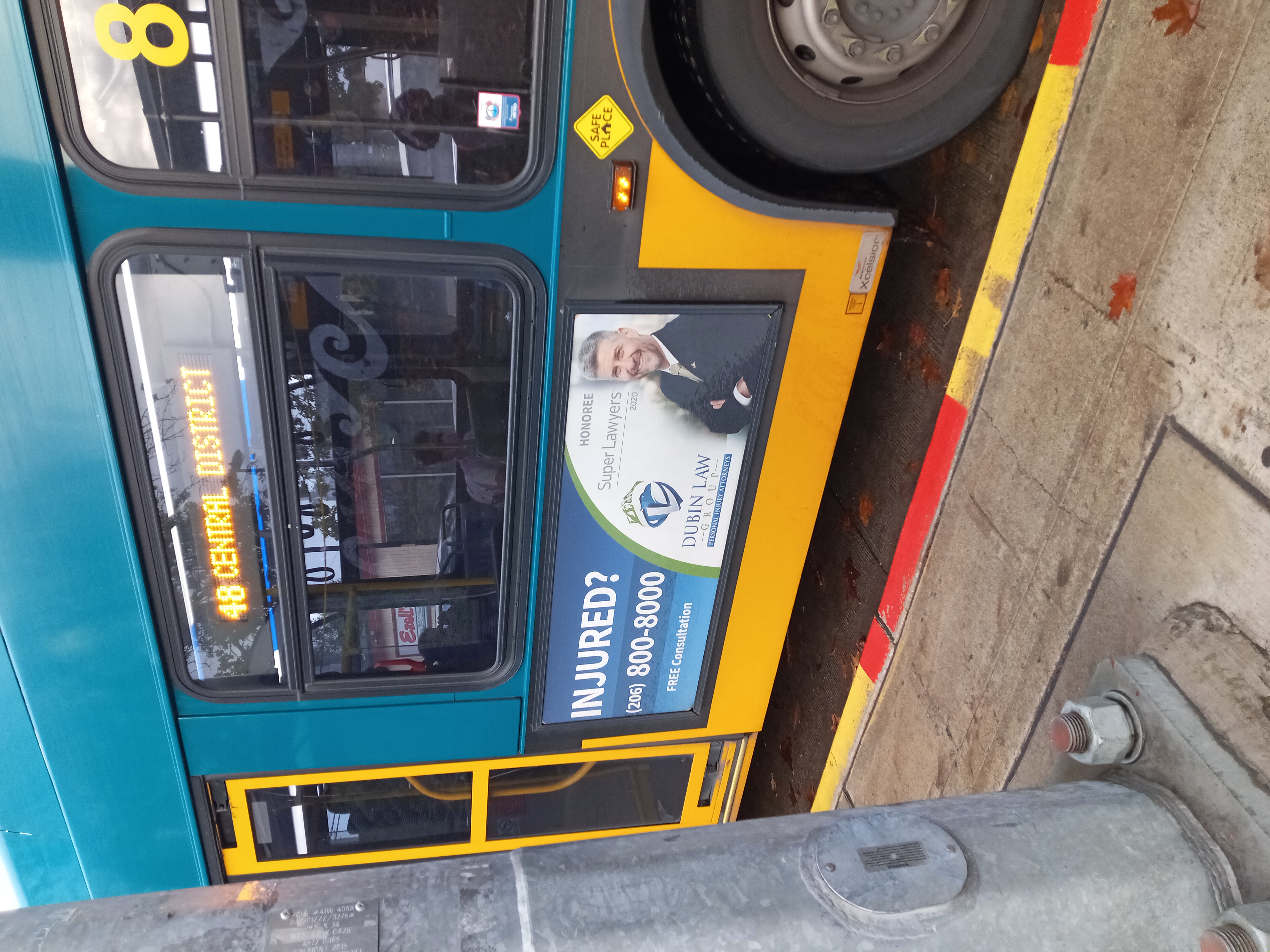 An image of the side of a King County Metro bus. Through the window, you can see a young person alone in a forward facing seat, wearing a pink mask.